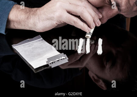 Sbuffare uomo bianco righe di farmaco con arrotolato dollar banconota sul buio con la riflessione Foto Stock