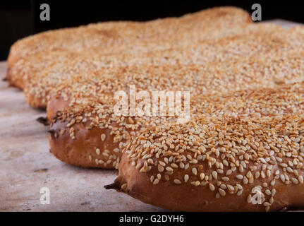 Ciambelle di sesamo in una fila su piastra in legno Foto Stock