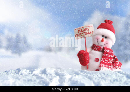 Pupazzo di neve con un cartellone in mano. Vestito con sciarpa rossa e guanti e hat nella neve fuori annunciando il natale Foto Stock