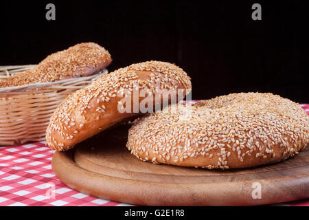 Round di sesamo bagel in cesto su tabella rossa e sfondo nero Foto Stock