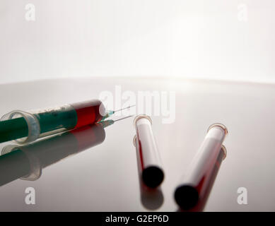 Siringa e fiale con il prelievo di campioni di sangue su bianco tavolo in vetro. Composizione orizzontale. Vista posteriore. Foto Stock