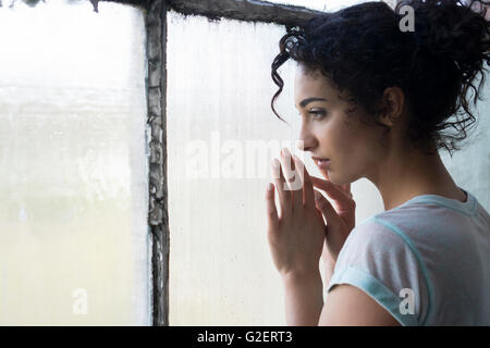 Triste giovane donna guardando fuori della finestra Foto Stock