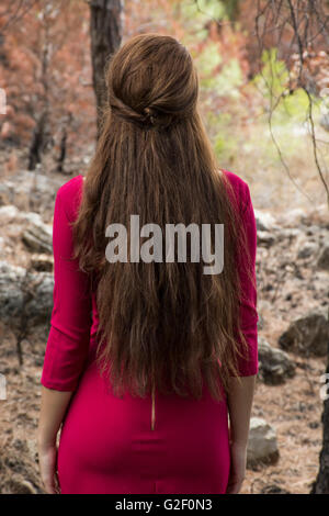 Giovane donna in abito rosso in piedi nella foresta Foto Stock