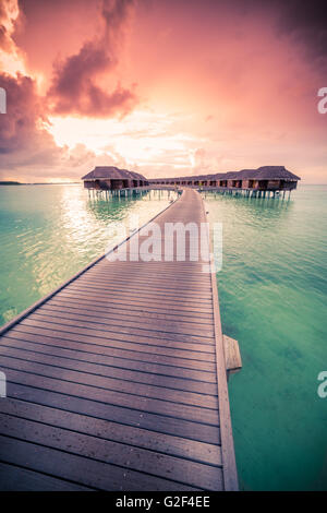 Incredibile sfondo astratto. Bel tramonto colori delle Maldive. Lungo pontile e lussuose ville overwater Foto Stock