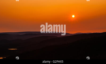 Sun al buio arancione tramonto splende sopra le linee di colline boscose rientranti nella lontana nebbia paesaggio, in Terranova, Canada. Foto Stock