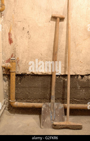 Vecchia pala e besom permanente al muro sporco Foto Stock