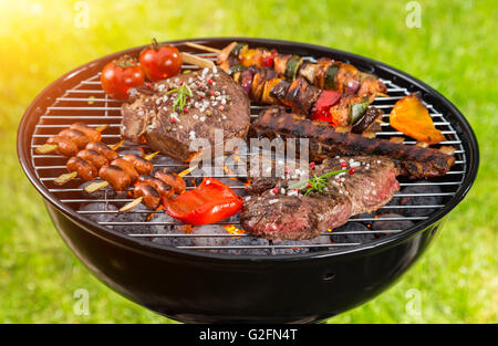 Vari tipi di carne servita sul grill con erba sullo sfondo Foto Stock