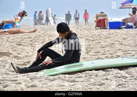 Una donna in una muta seduto sulla spiaggia accanto alla sua tavola da surf Foto Stock