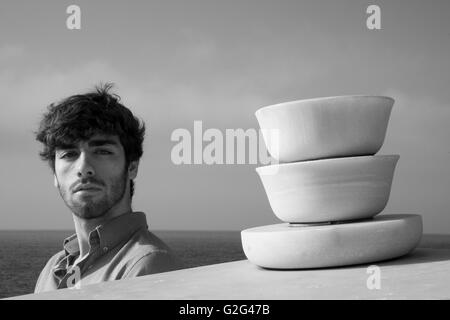 Testa e spalle Ritratto di giovane uomo adulto nei pressi di scultura astratta con Ocean in background Foto Stock