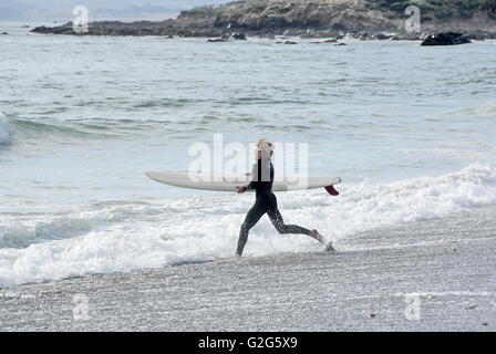 Surfer in esecuzione su Pietra di luna beach nella città di Cambria, California Foto Stock