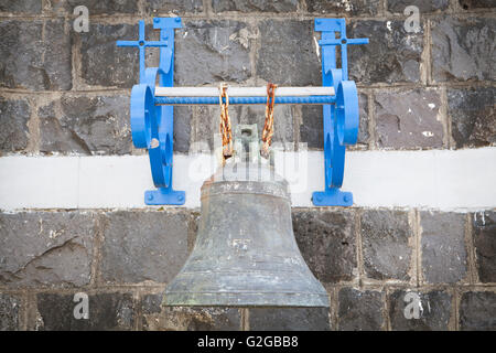 Vecchia chiesa campana sulla parete e telaio blu detenute da due catene arrugginito Foto Stock