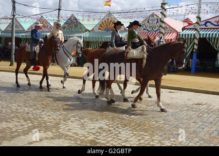 Siviglia Spagna Feria 2016 donne equitazione sella laterale passato casetas uomini seguenti abito tradizionale Foto Stock