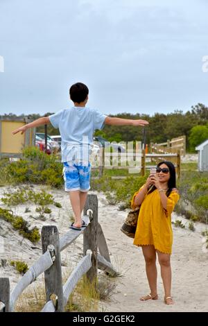 Un giovane ragazzo cerca di equilibrio come egli cammina attraverso la parte superiore di una recinzione di legno in spiaggia Foto Stock