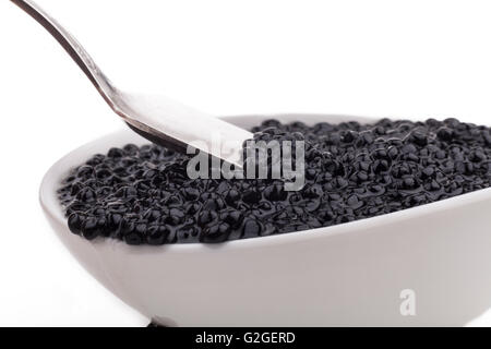 Il caviale nero di perline in ciotola bianco e silver spoon di close-up isolati su sfondo bianco Foto Stock