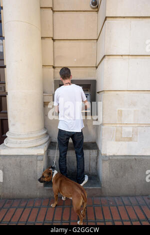 L'uomo con il suo cane al guinzaglio utilizza un bancomat in macchina Chelmsford Essex Inghilterra Foto Stock