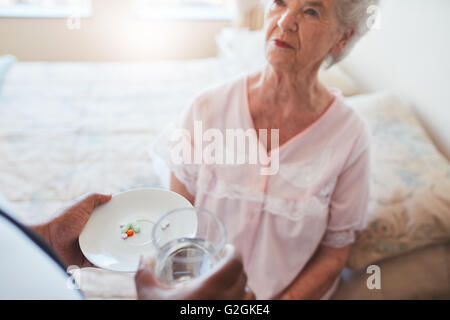 Senior donna seduta sul letto e home care nurse dando farmaco. La mano di infermiere dando pillole per anziani paziente femmina. Foto Stock