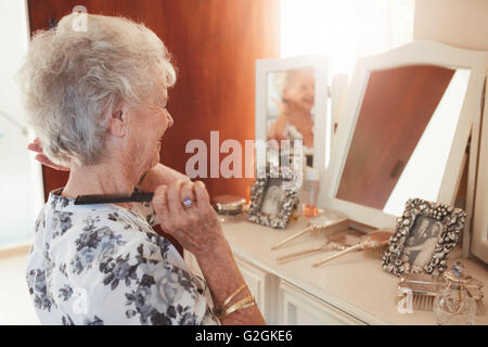 Felice donna senior pettinare i capelli a cassettiera in casa. Femmina anziani preparano davanti a uno specchio a casa. Foto Stock