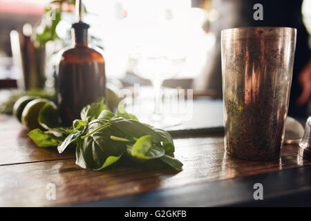 Closeup colpo di foglie di basilico con shaker e altri ingredienti sul tavolo al bar. Foto Stock