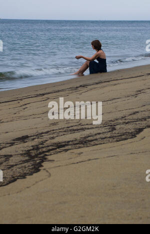 Giovane donna di vagliatura sabbia attraverso le mani sulla spiaggia Foto Stock