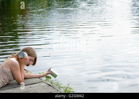 Giovane donna adulta ascoltando la scatoletta di latta a bordo d'acqua Foto Stock