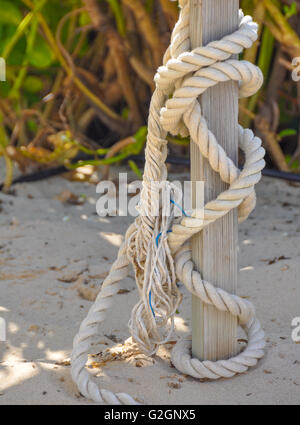 Il vecchio la corda avvolta intorno ad un palo che è circondato da sabbia, spiaggia Foto Stock