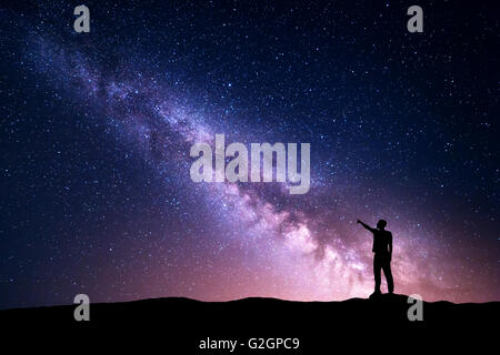 La Via Lattea con la silhouette di una levatura giovane di puntare il dito nella notte cielo stellato sulla montagna. Paesaggio notturno Foto Stock