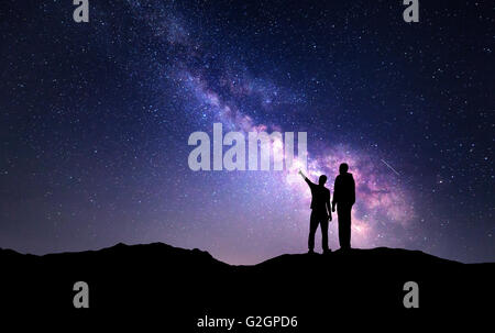 La Via Lattea con la silhouette di una famiglia in montagna. Padre e figlio che puntare il dito nella notte cielo stellato. Paesaggio notturno Foto Stock