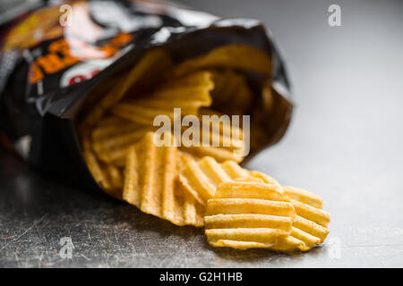 Crinkle cut potato chips sul vecchio tavolo da cucina. Patate fritte riversato da imballaggio. Foto Stock