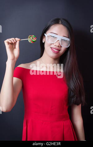 Bella donna tenendo un lecca-lecca mentre indossa l'abito rosso Foto Stock