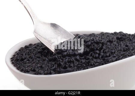 Il caviale nero di perline in ciotola bianco e silver spoon di close-up isolati su sfondo bianco Foto Stock