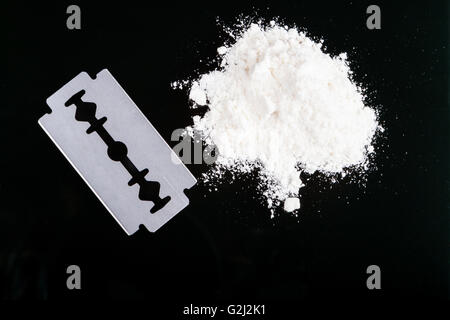 Una lama di rasoio closeup bianco con polvere di farmaco su sfondo nero con la riflessione Foto Stock
