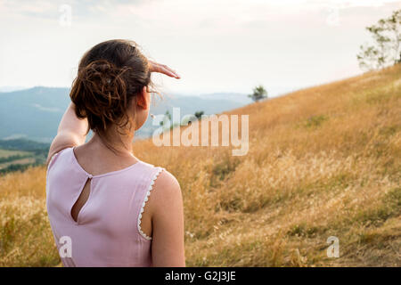 In primo piano della donna in abito rosa guardando fuori nella distanza in campo, vista posteriore Foto Stock