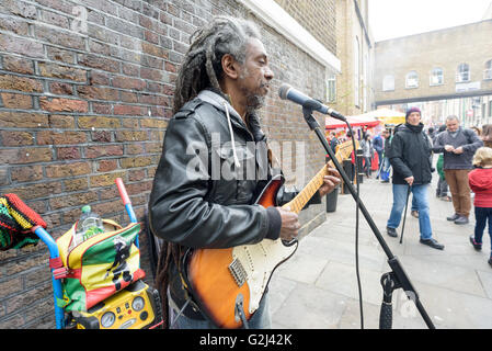 Un suonatore ambulante di strada Gioca denaro con una chitarra elettrica per le donazioni a Brick Lane a Londra durante il primo maggio del Bank Holiday Foto Stock