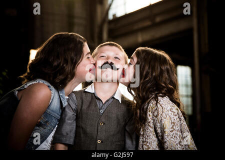 Due ragazze baciare Ragazzo con labbra di cera in magazzino abbandonato Foto Stock