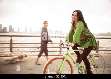 Ritratto di donna sorridente in bicicletta vicino al fiume, New York City, Stati Uniti d'America Foto Stock