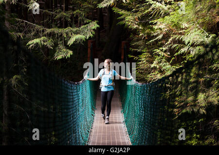 Giovane donna escursionista sulla sospensione ponte tra la Cina e la spiaggia Spiaggia di mistica lungo Juan de Fuca Trail Isola di Vancouver BC Canada. Foto Stock