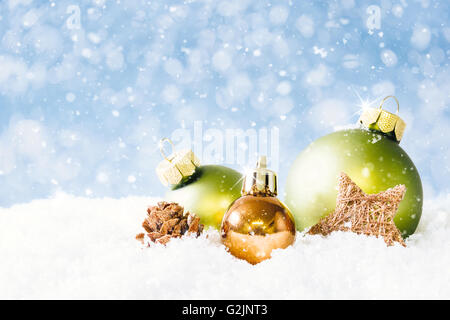 Un cono di fuoco e tre palle di Natale sulla neve con morbido blu bokeh di fondo e la caduta di neve. Foto Stock