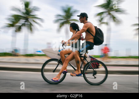 RIO DE JANEIRO - Marzo 6, 2016: surfista brasiliano prende una tavola da surf e amico su una bicicletta sul fronte spiaggia di Ipanema street. Foto Stock