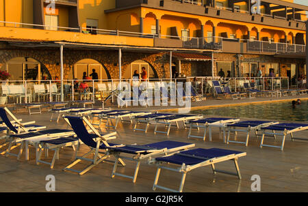 Palazzo arancione sdraio blu suns nel tardo pomeriggio bassa raggi riflettendo su hotel front ombre a bordo piscina. Foto Stock