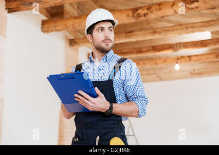 Malinconici builder in hardhat con appunti e matita in ambienti interni Foto Stock