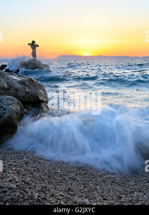 Statua di una donna sulla roccia al tramonto in Podgora, Riviera di Makarska, Croazia Foto Stock