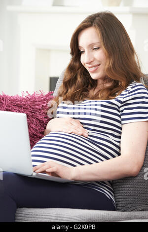 Donna incinta utilizzando portatile a casa Foto Stock