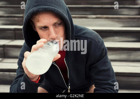 Urban sportman riposo dopo la sessione di allenamento seduta sulle scale. Acqua potabile Foto Stock