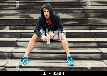 Urban sportivo a riposo dopo l'allenamento, seduta sulle scale. Acqua potabile Foto Stock