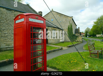 Defibrillatore mantenuta in un tradizionale in disuso telefono rosso scatola per uso in emergenza nel villaggio di Slingsby, North Yorkshire, Regno Unito Foto Stock