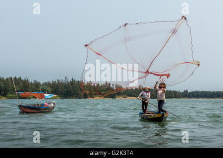 I pescatori locali di gettare le reti da pesca da barche sul fiume, Hoi An, Vietnam Foto Stock