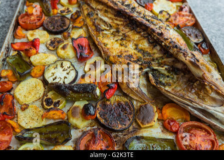 Primo piano di squisiti piatti a base di pesce al forno con pomodori arrostiti, patate e ortaggi Foto Stock