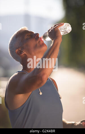 Bello il senior jogging uomo di bere acqua fresca da una bottiglia dopo mornig eseguire Foto Stock