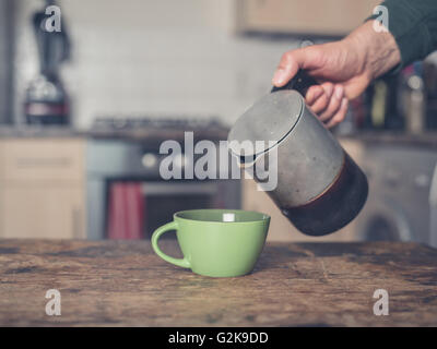 Un maschio di mano è versare il caffè in una tazza in una cucina da una moka Caffettiera espresso Foto Stock