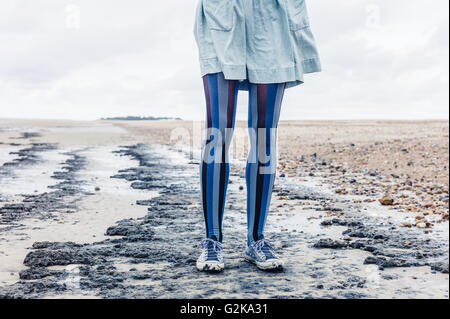 Le gambe di una giovane donna come lei è in piedi sulla spiaggia con il suo mantello al vento Foto Stock